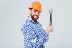 A smiling bearded plumber wearing a helmet and holding a wrench, ready to tackle various plumbing tasks