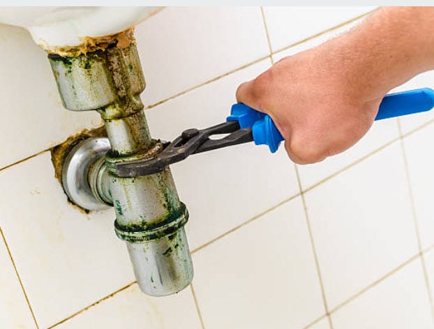 A plumber fixing a pipe under a sink, demonstrating proper plumbing maintenance techniques