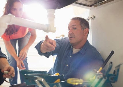 A plumber fixing a pipe under the kitchen sink, demonstrating effective plumbing maintenance techniques